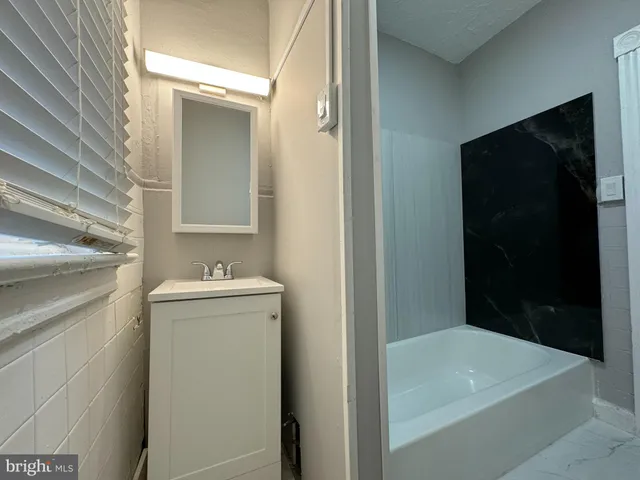 a bathroom with a granite countertop sink and mirror with bathtub