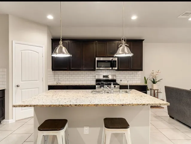 a kitchen with stainless steel appliances granite countertop a sink a stove a microwave a center island and chairs