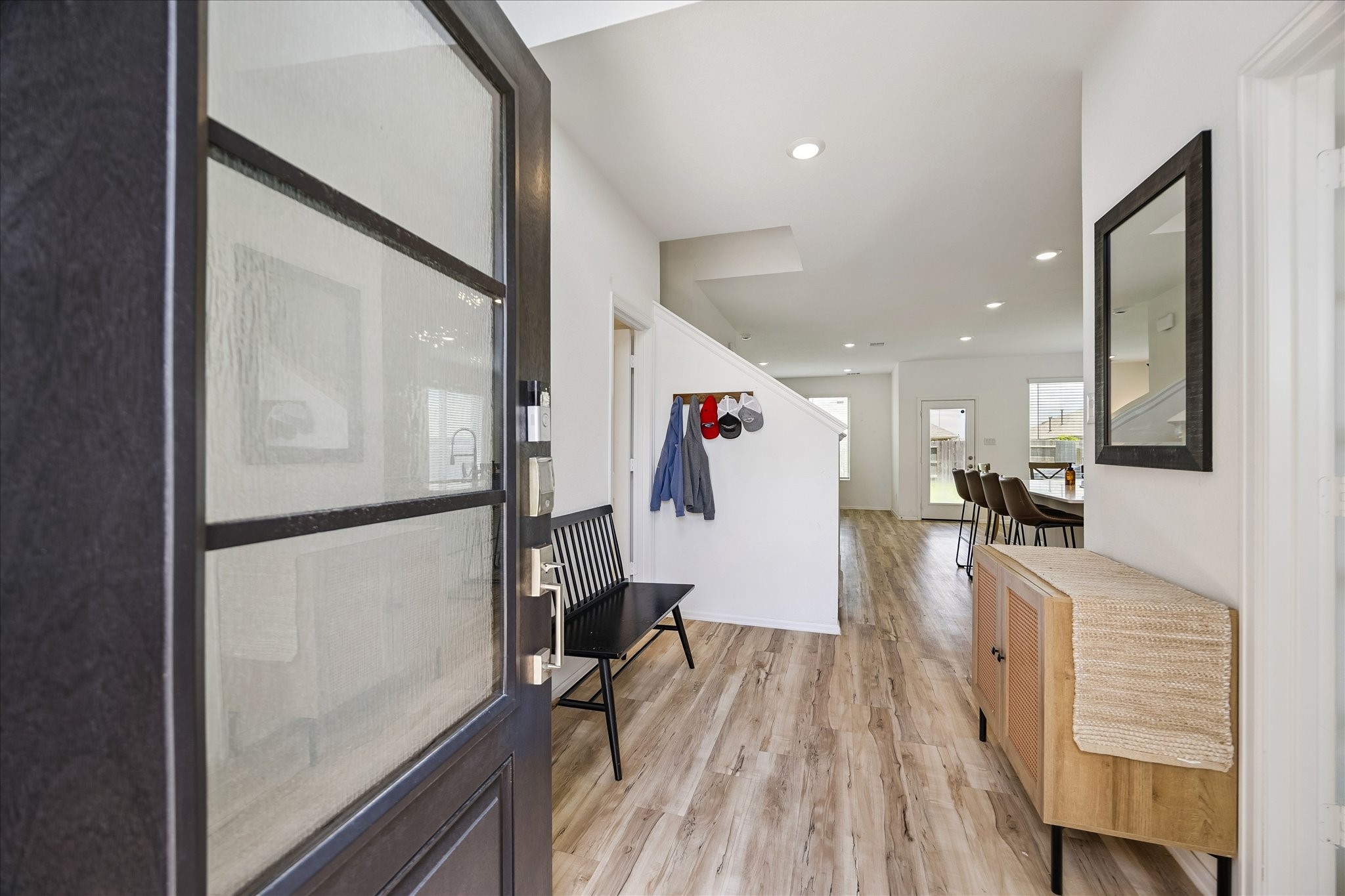 3812 Moss Hl Road Rosenberg, TX 77469 - Photo 7 of 20 Welcome to a bright, inviting entryway with modern wood flooring that flows into an open living space. The area features coat hooks, providing functionality and charm. Natural light enhances the clean, contemporary design, leading seamlessly to the dining area and beyond.