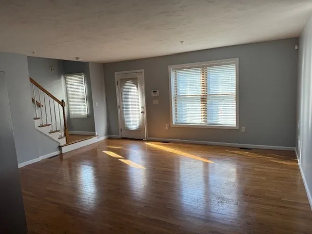 a view of an empty room with wooden floor and fan