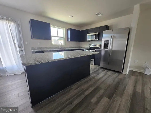 a kitchen with granite countertop a refrigerator a sink a stove and cabinets