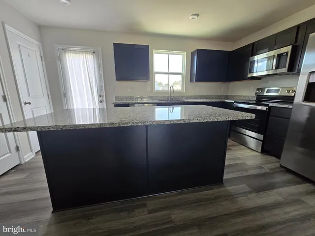 a kitchen with granite countertop a refrigerator a stove a sink and dishwasher with wooden floor