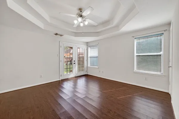 an empty room with wooden floor chandelier fan and windows