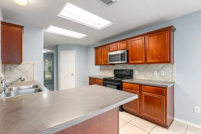 a kitchen with stainless steel appliances granite countertop wooden cabinets a sink and dishwasher a stove top oven with wooden floor