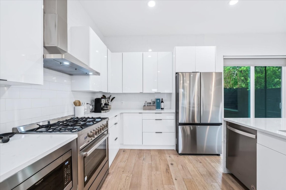6300 Santos Street, Unit 3 Austin, TX 78741 - Photo 13 of 32 a kitchen with a refrigerator a sink dishwasher a stove and white cabinets with wooden floor