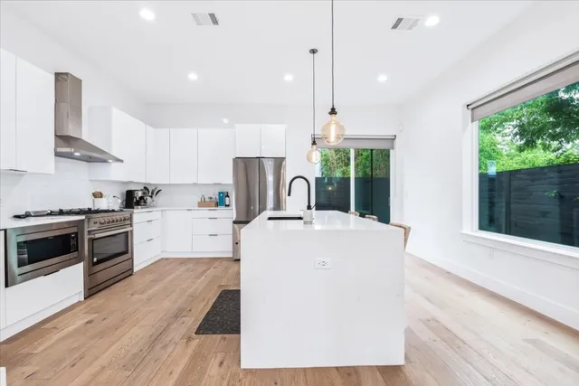 a large kitchen with stainless steel appliances a stove a sink dishwasher a refrigerator white cabinets and wooden floor next to a window