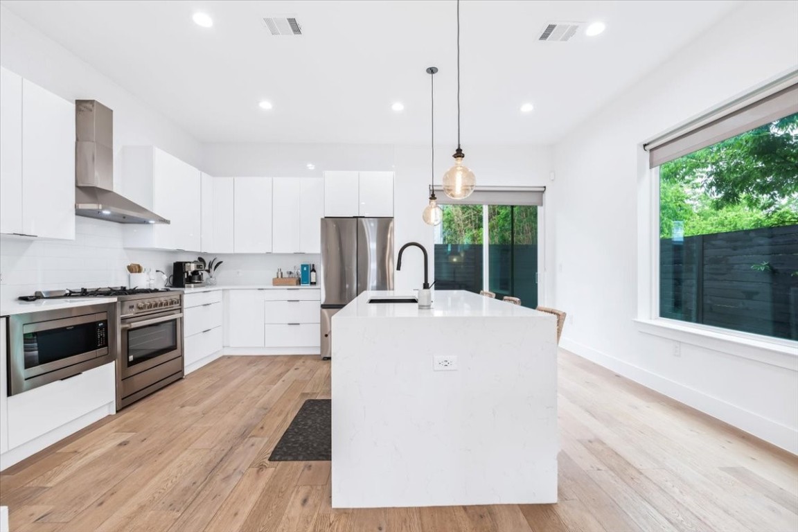6300 Santos Street, Unit 3 Austin, TX 78741 - Photo 7 of 32 a large kitchen with stainless steel appliances a stove a sink dishwasher a refrigerator white cabinets and wooden floor next to a window