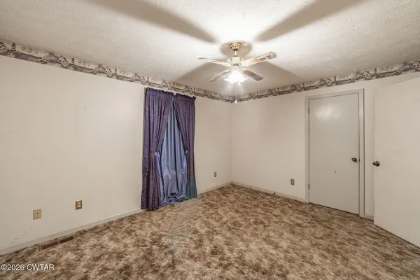 an empty room with chandelier fan and windows