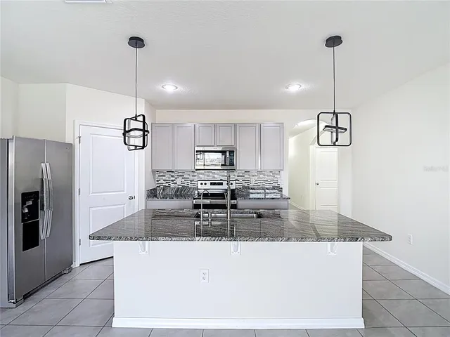a kitchen with stainless steel appliances kitchen island granite countertop a refrigerator a stove and white cabinets