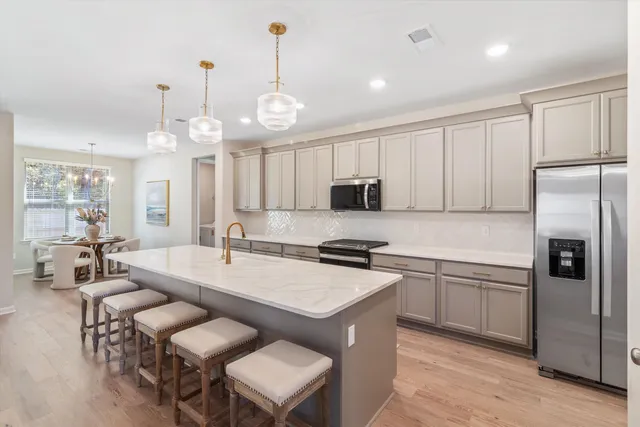 a large kitchen with granite countertop a stove a sink a refrigerator and a living room view