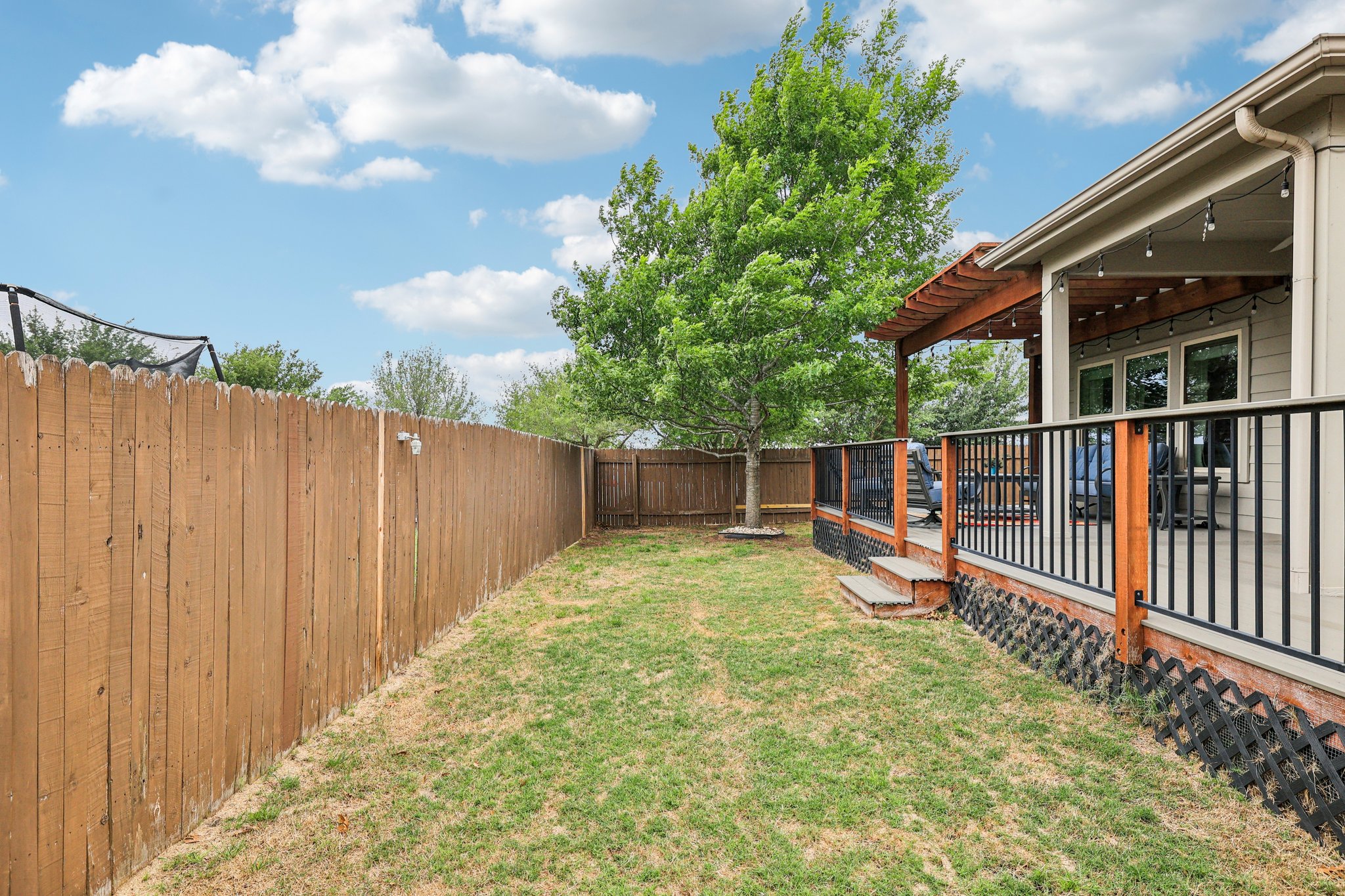 10033 Gertrudis Loop Austin, TX 78747 - Photo 26 of 39 The property features a fenced yard with a lawn, a mature tree, and a covered patio area with string lights and a black railing