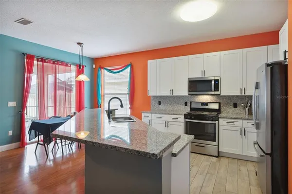 a kitchen with stainless steel appliances granite countertop a stove top oven a sink dishwasher a refrigerator and a dining table with wooden floor