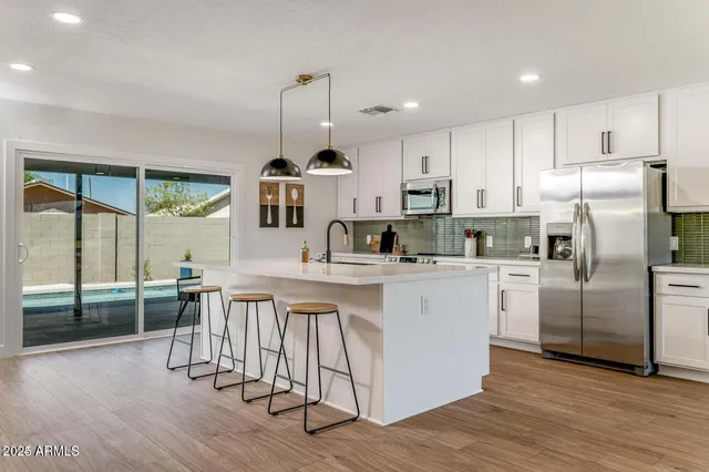 a kitchen with stainless steel appliances granite countertop a refrigerator a sink dishwasher a stove and white cabinets with wooden floor