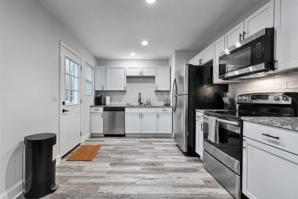 a kitchen with stainless steel appliances granite countertop a refrigerator a stove top oven a sink dishwasher and white cabinets with wooden floor