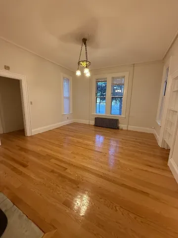 an empty room with wooden floor chandelier and windows
