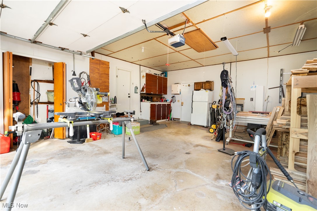 659 Lake Road Conneaut, OH 44030 - Photo 16 of 24 Garage featuring a workshop area, a garage door opener, and white fridge