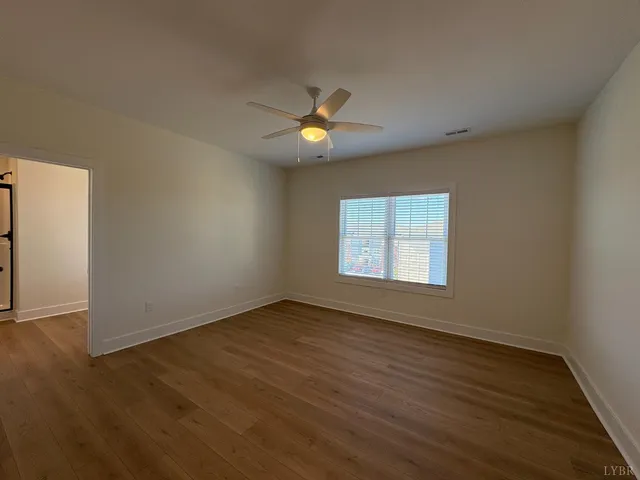 an empty room with wooden floor chandelier fan and windows