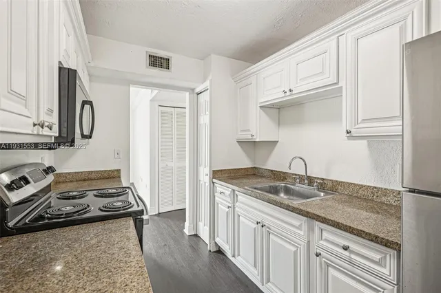a kitchen with stainless steel appliances granite countertop a sink stove oven and white cabinets with wooden floor