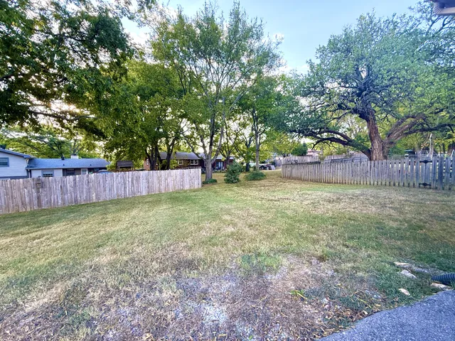 a view of a backyard with large trees and wooden fence