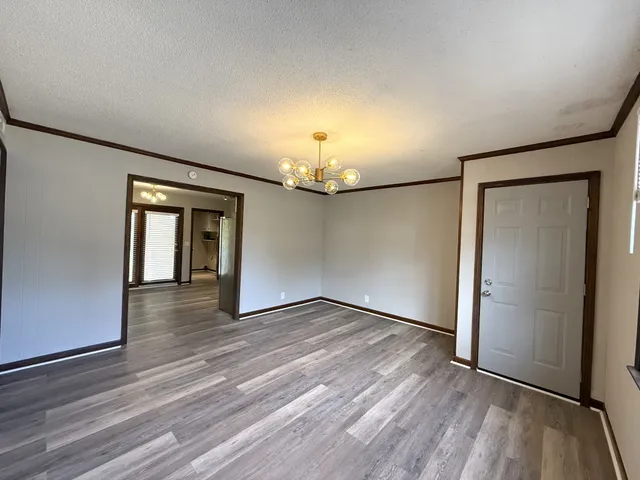 an empty room with wooden floor chandelier and windows