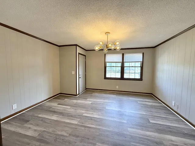 an empty room with wooden floor chandelier and windows