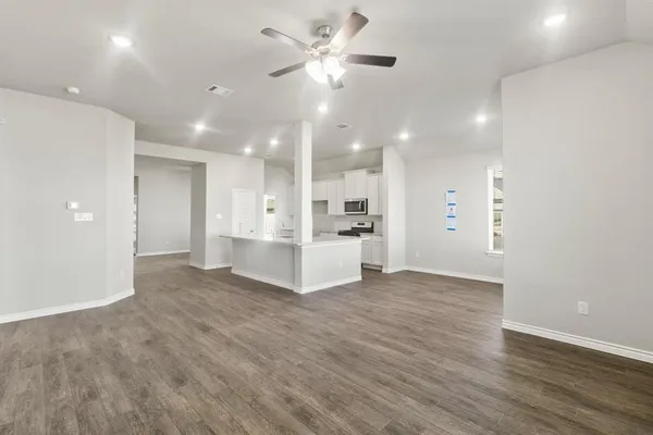 a view of an empty room and kitchen with wooden floor