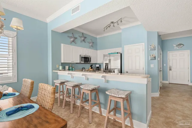 a kitchen with stainless steel appliances kitchen island granite countertop a dining table chairs and a refrigerator