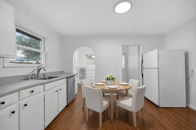 a kitchen with stainless steel appliances granite countertop a dining table chairs and white cabinets with wooden floor