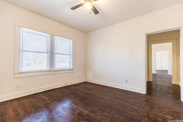 an empty room with wooden floor chandelier fan and windows