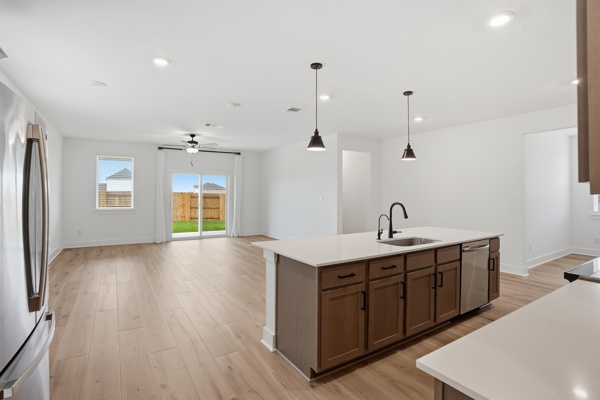 201 Prodigal Way Kyle, TX 78640 - Photo 19 of 22 Open concept kitchen and living area featuring light wood flooring, a central kitchen island with a sink and pendant lighting, and a sliding glass door leading to a fenced yard