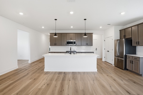 201 Prodigal Way Kyle, TX 78640 - Photo 20 of 22 The kitchen features a central island with a sink, pendant lighting, stainless steel appliances, and wood-look flooring