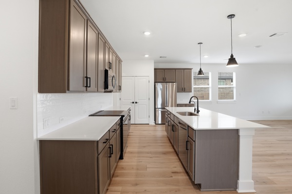 201 Prodigal Way Kyle, TX 78640 - Photo 5 of 22 The kitchen features stylish cabinetry, stainless steel appliances, a white tile backsplash, and a central island with a sink and pendant lighting