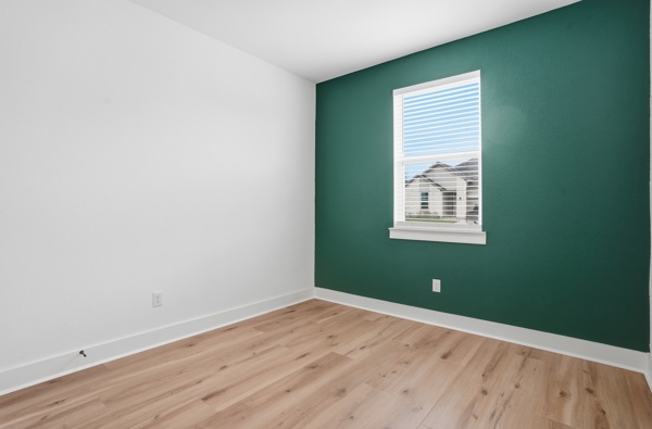 201 Prodigal Way Kyle, TX 78640 - Photo 7 of 22 The room features light-toned wood flooring, a window with blinds, and a striking accent wall in a deep green hue