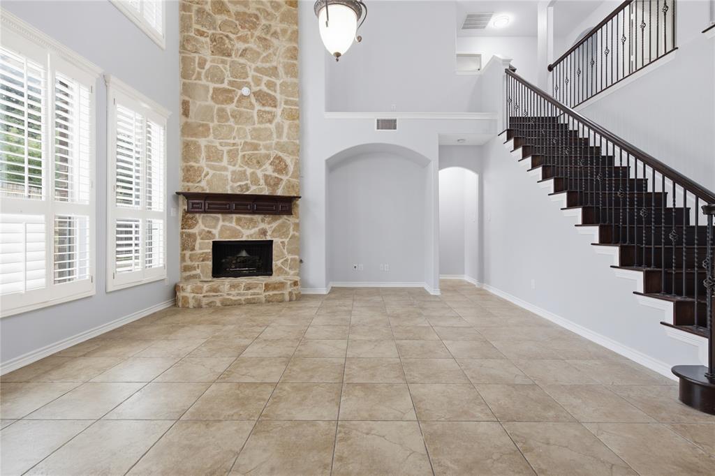 10001 Thurman Road Fort Worth, TX 76244 - Photo 8 of 40 Spacious living area featuring a stone-clad fireplace with a dark wood mantel, high ceilings, large windows with plantation shutters, and light-toned tile flooring