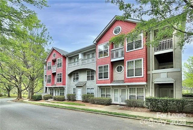 a front view of a multi story residential apartment building with yard and parking