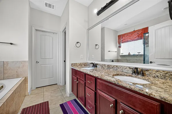 a bathroom with a granite countertop double vanity sink a mirror and a bathtub