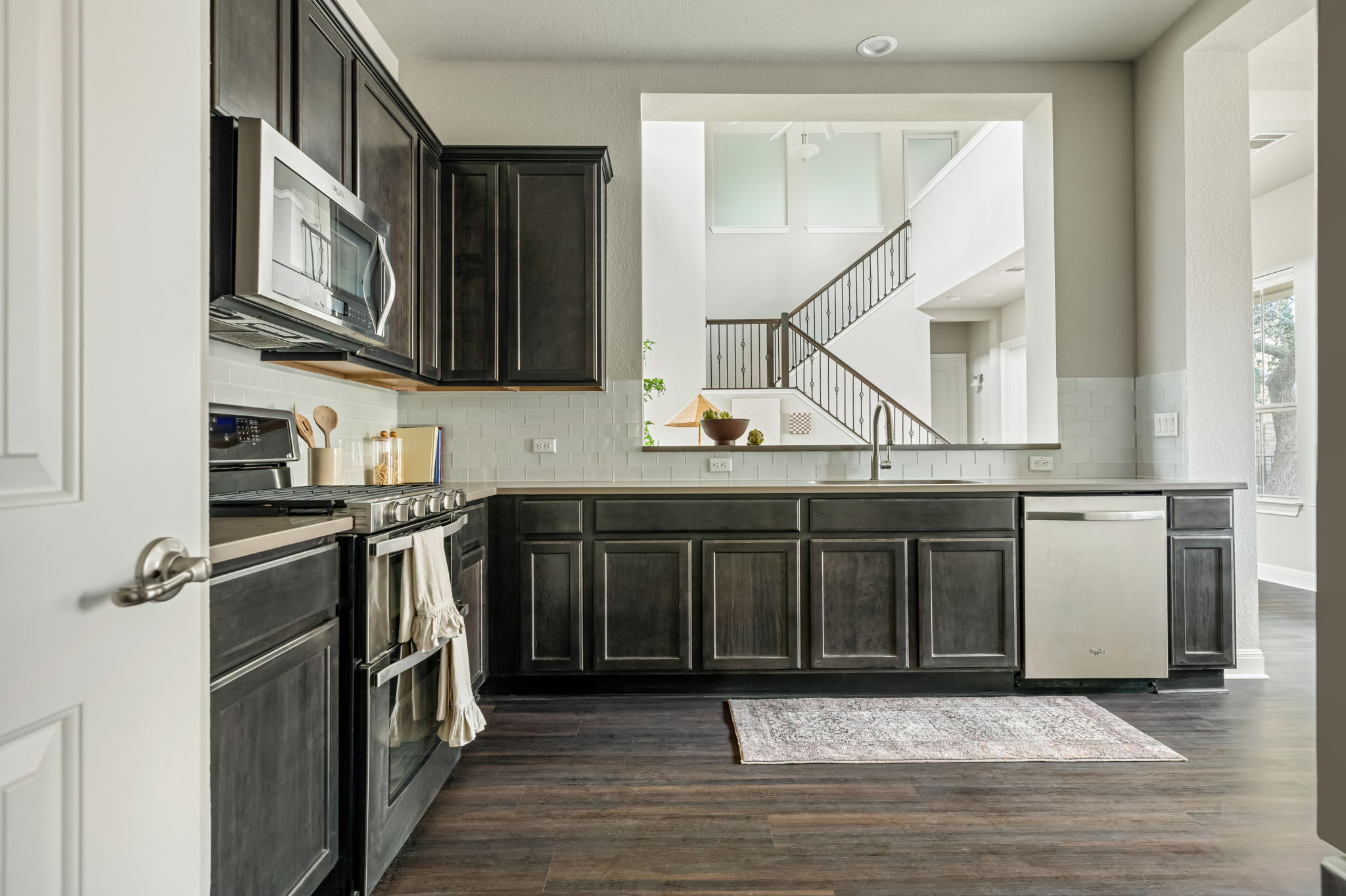2516 Hopsack Mills Road Austin, TX 78748 - Photo 13 of 39 Kitchen featuring dark wood-finish cabinetry, stainless steel appliances, light-toned countertops, a white subway tile backsplash, and wood-finish flooring
