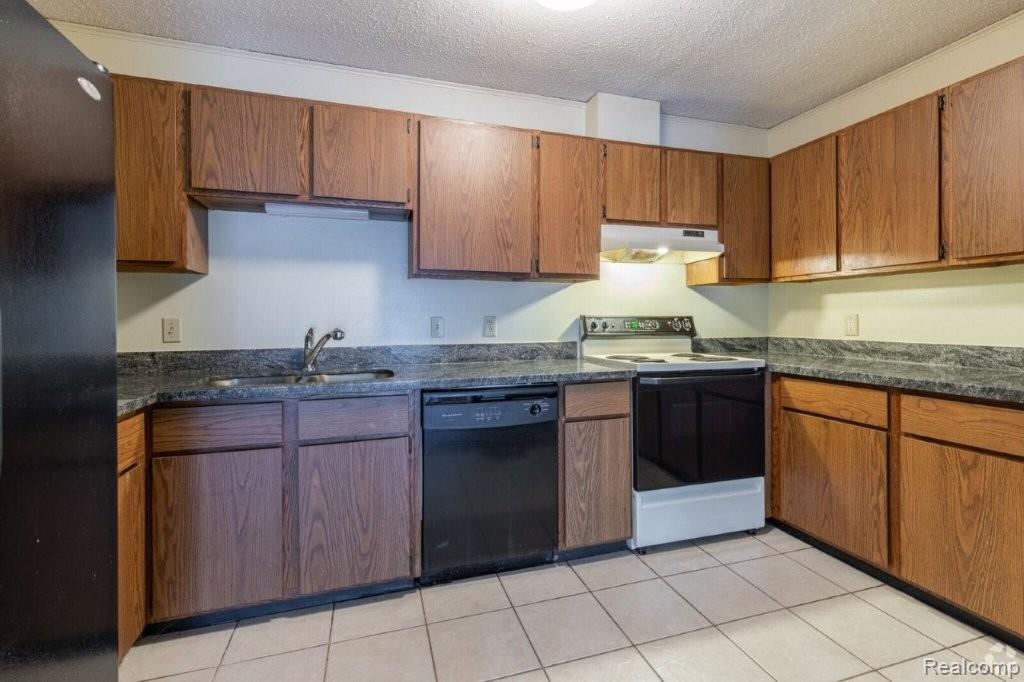 35775 Union Lake Road Clinton Township, MI 48035 - Photo 14 of 30 Kitchen with black appliances, a textured ceiling, brown cabinets, light tile patterned floors, and under cabinet range hood