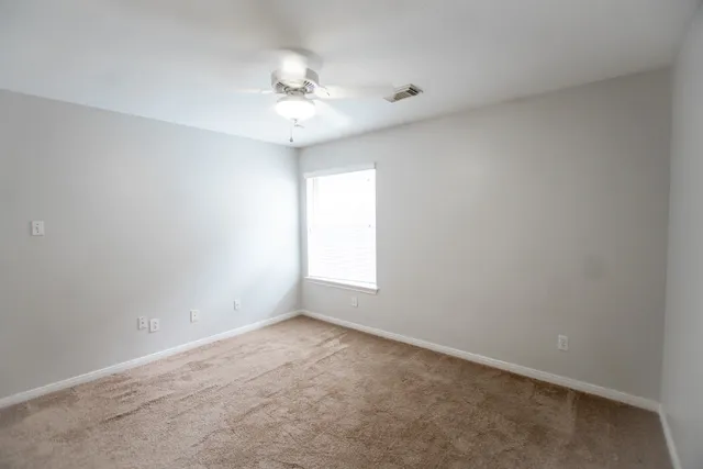 an empty room with a chandelier fan and windows