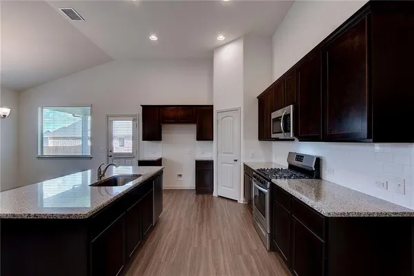 a kitchen with stainless steel appliances wooden cabinets granite counter tops a stove a sink and a microwave
