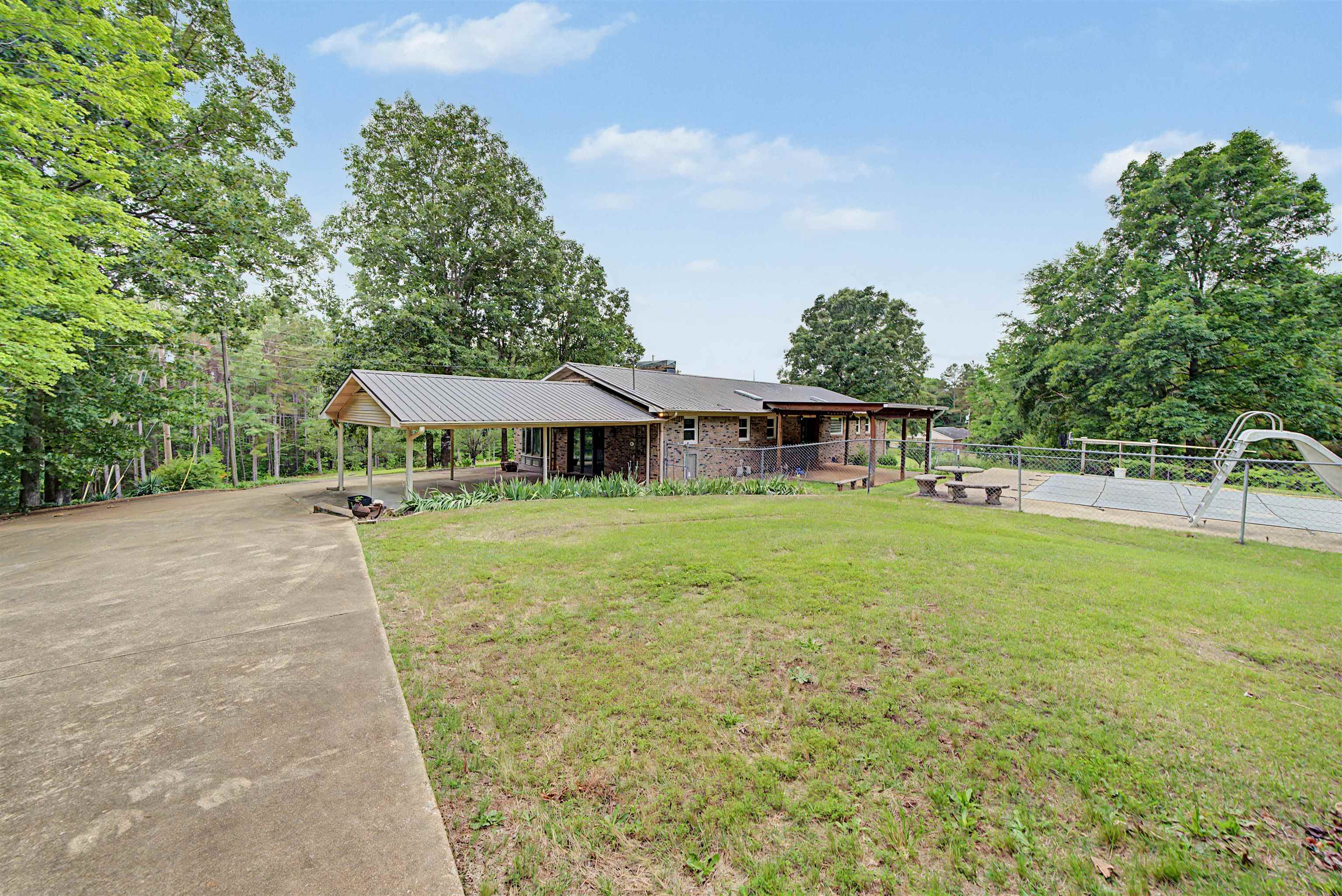 436 Skyline Road Selmer, TN 38375 - Photo 18 of 40 Expansive concrete driveway leading to a residence featuring a covered carport, stone-clad exterior, and a metal roof