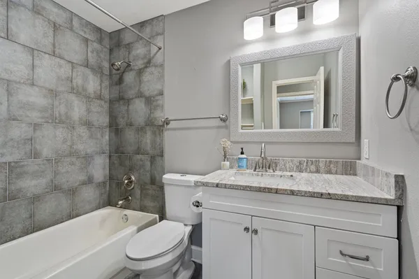 a bathroom with a granite countertop bathtub shower sink vanity mirror and toilet