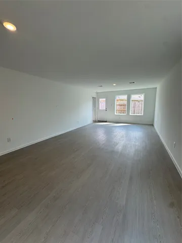 a view of an empty room with wooden floor and windows