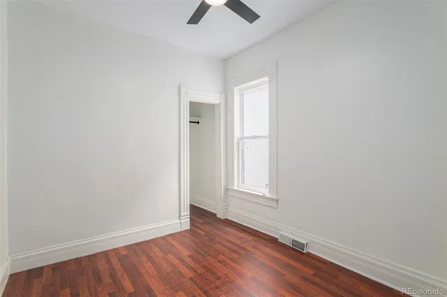 an empty room with wooden floor chandelier fan and windows
