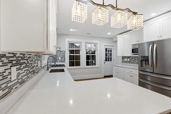 a large white kitchen with a window and refrigerator