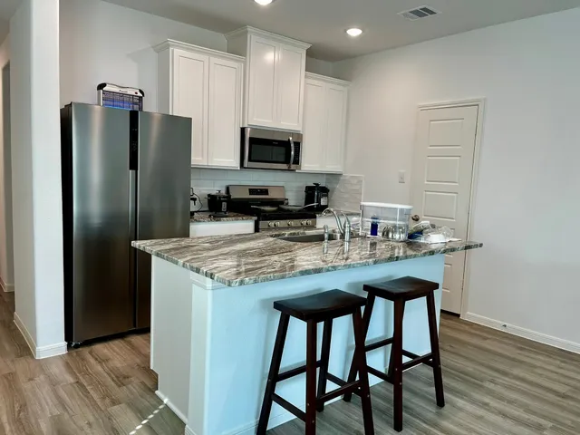 a kitchen with stainless steel appliances granite countertop a dining table chairs refrigerator and microwave