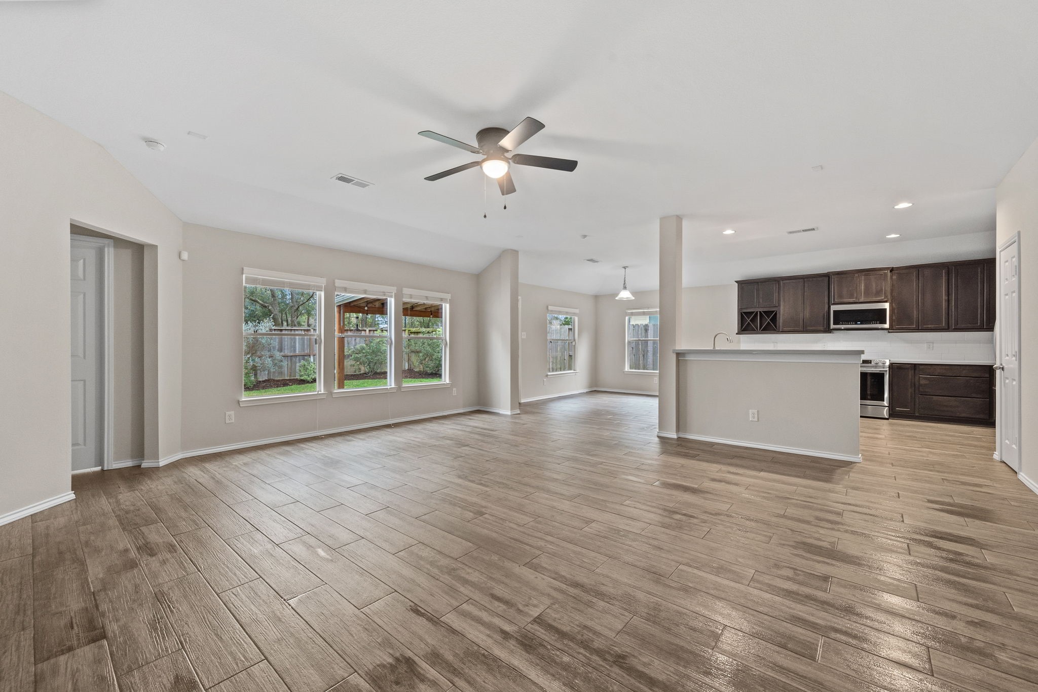 1910 Katlyn Lane Spring, TX 77386 - Photo 9 of 35 This open-concept living area features wood-look tile flooring, abundant natural light from large windows, and a modern UPDATED KITCHEN. The space is highlighted by a ceiling fan and neutral tones, offering a spacious and inviting atmosphere.
