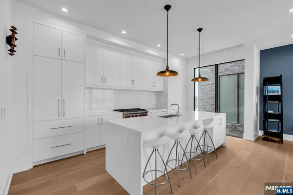 a kitchen with stainless steel appliances a stove a refrigerator a sink and white cabinets with wooden floor