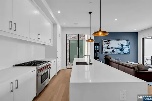 a kitchen with stainless steel appliances a stove a sink a refrigerator and white cabinets with wooden floor