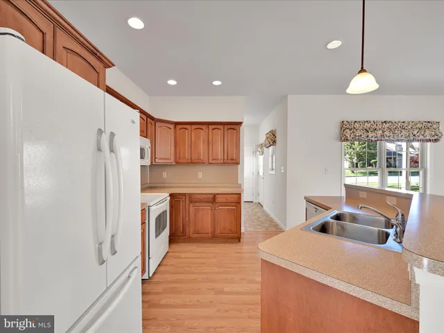 a kitchen with stainless steel appliances granite countertop a refrigerator a sink dishwasher a stove and white countertops with wooden floor